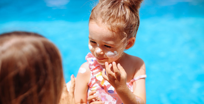 mother helping child dab on sunblock 943x481