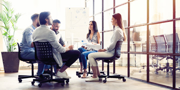 Informal team meeting with 5 colleagues sat on chairs in open office