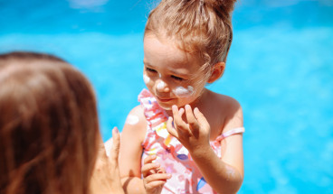 mother helping child dab on sunblock 767x418