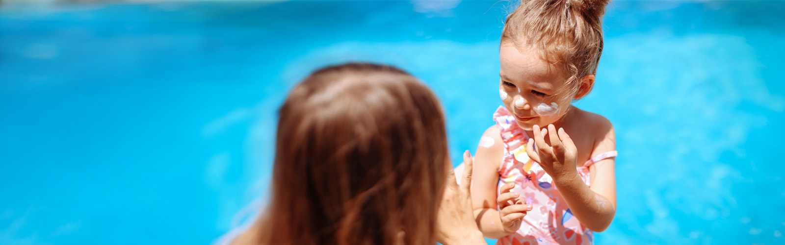 child putting on sunscreen next to a pool 1600x500