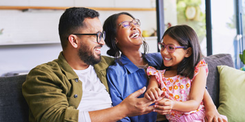 Parents laughing together with young daughter while sitting on sofa